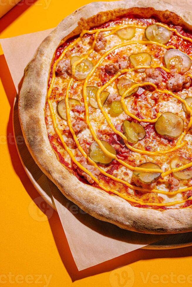 Delicious pizza topped with pickles and drizzle, served on a bright yellow background photo