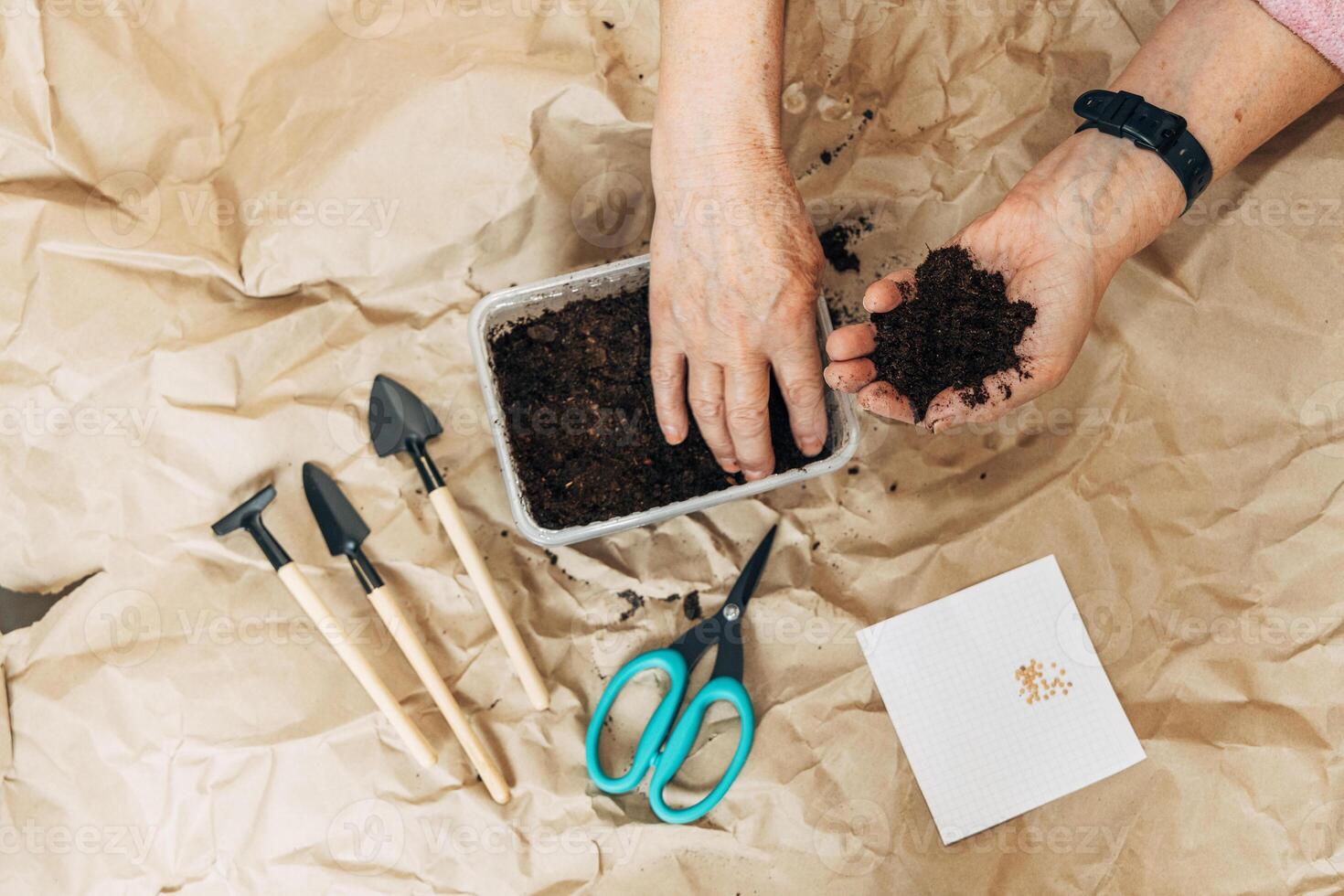 Kraft paper background, fertile soil and garden tools, top view. Hands planting seeds photo