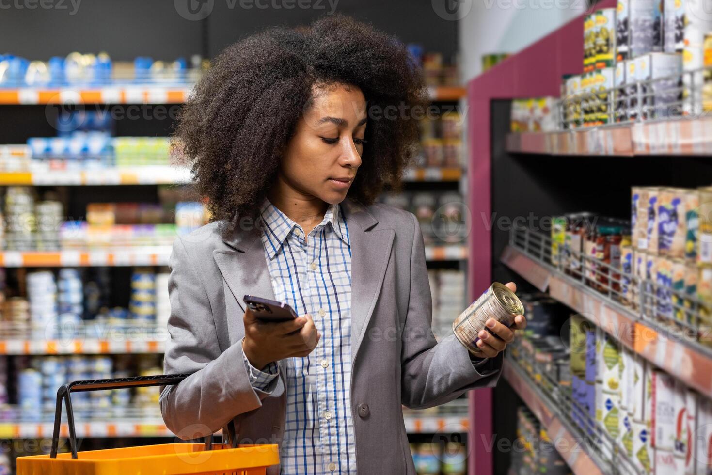 A young African-American woman in a suit is standing at a grocery counter in a supermarket, holding a metal can and choosing a product. photo