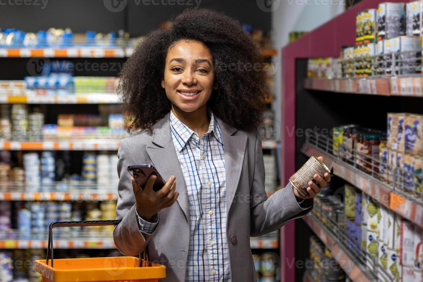A cheerful woman smiles while shopping in a grocery store. She holds a canned food item in one hand and a smartphone in the other. The image captures the convenience of modern retail experiences. photo