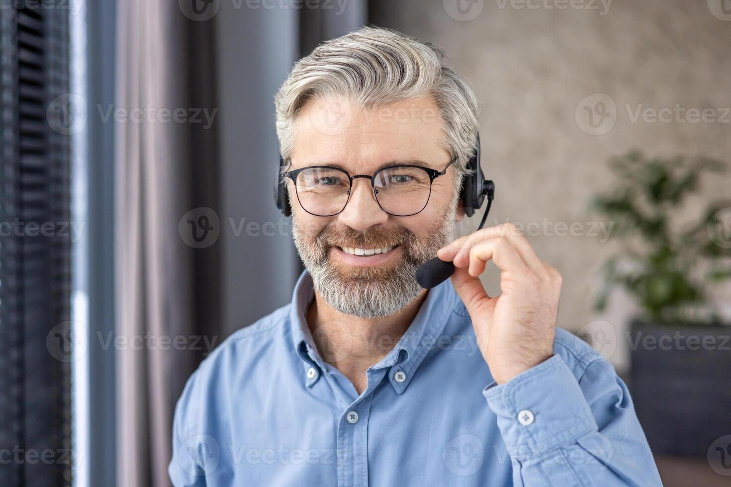 Smiling mature man with glasses wearing a headset in an office setting, portraying friendly customer service and professionalism. photo