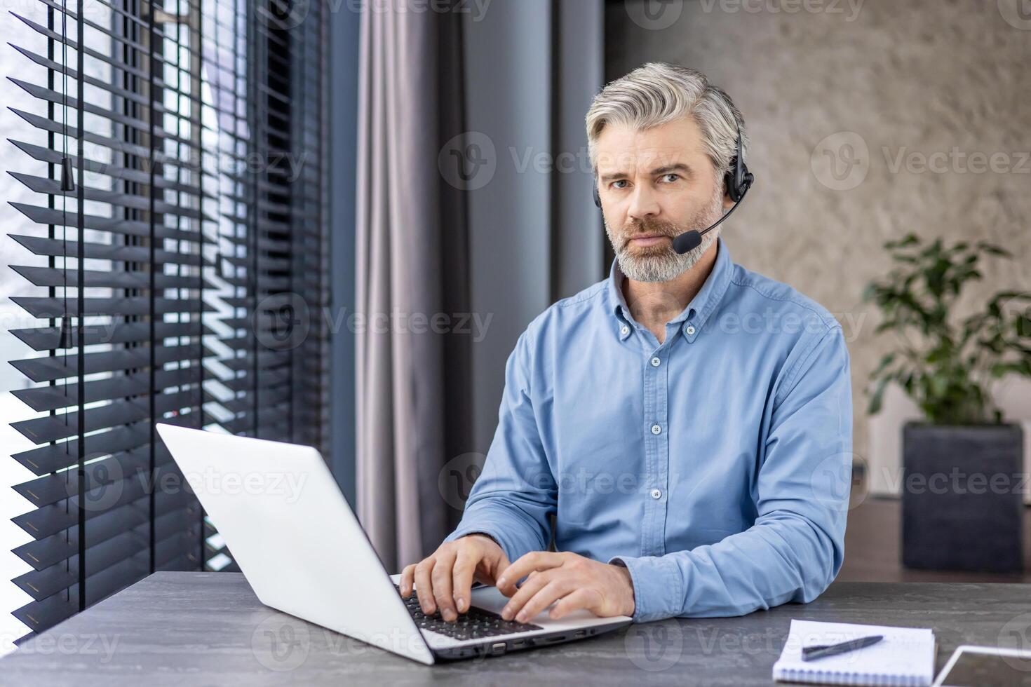 Professional middle-aged man with headset working on laptop in a modern office setting, showcasing focus and efficiency. photo