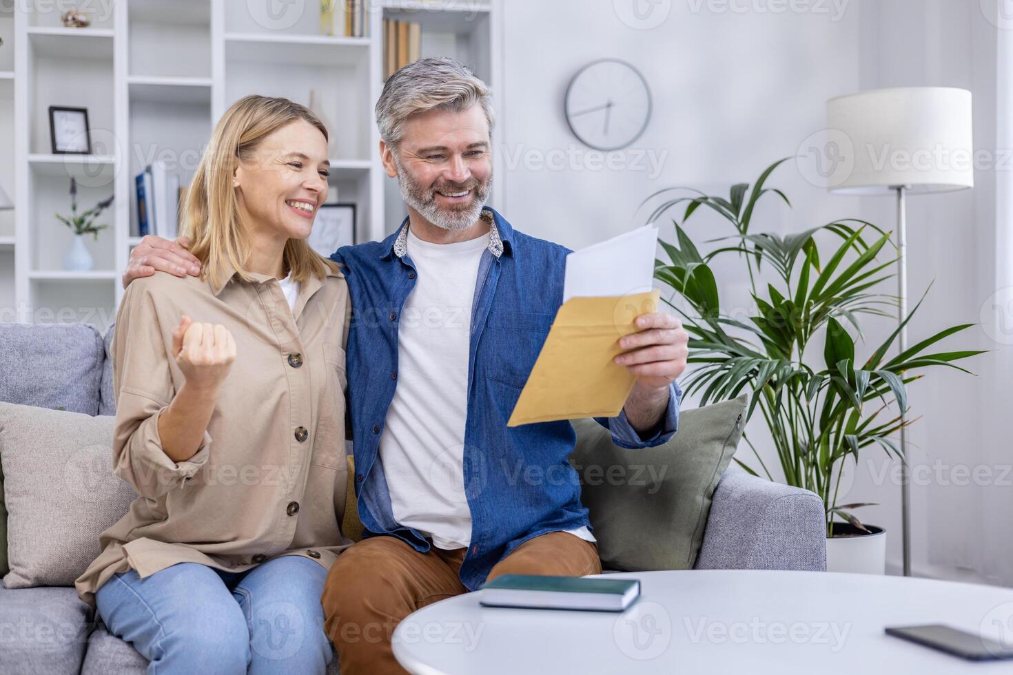 Happy couple celebrating with documents in hand at home. They are smiling and expressing excitement while sitting on the sofa in a cozy living room. photo