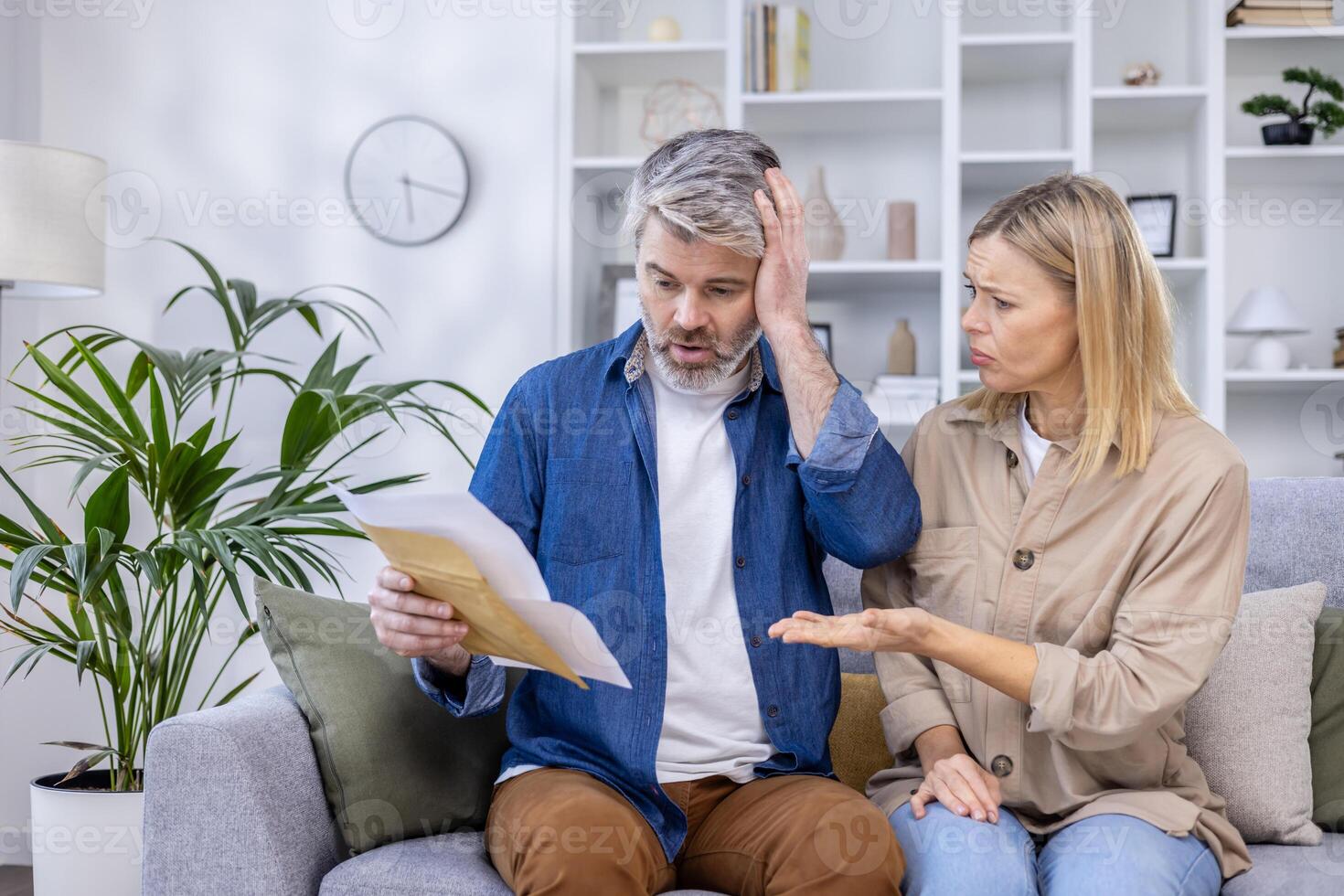 A stressed couple reviewing their finances and bills while sitting on a sofa at home. The image conveys worry, stress, and financial problems. photo