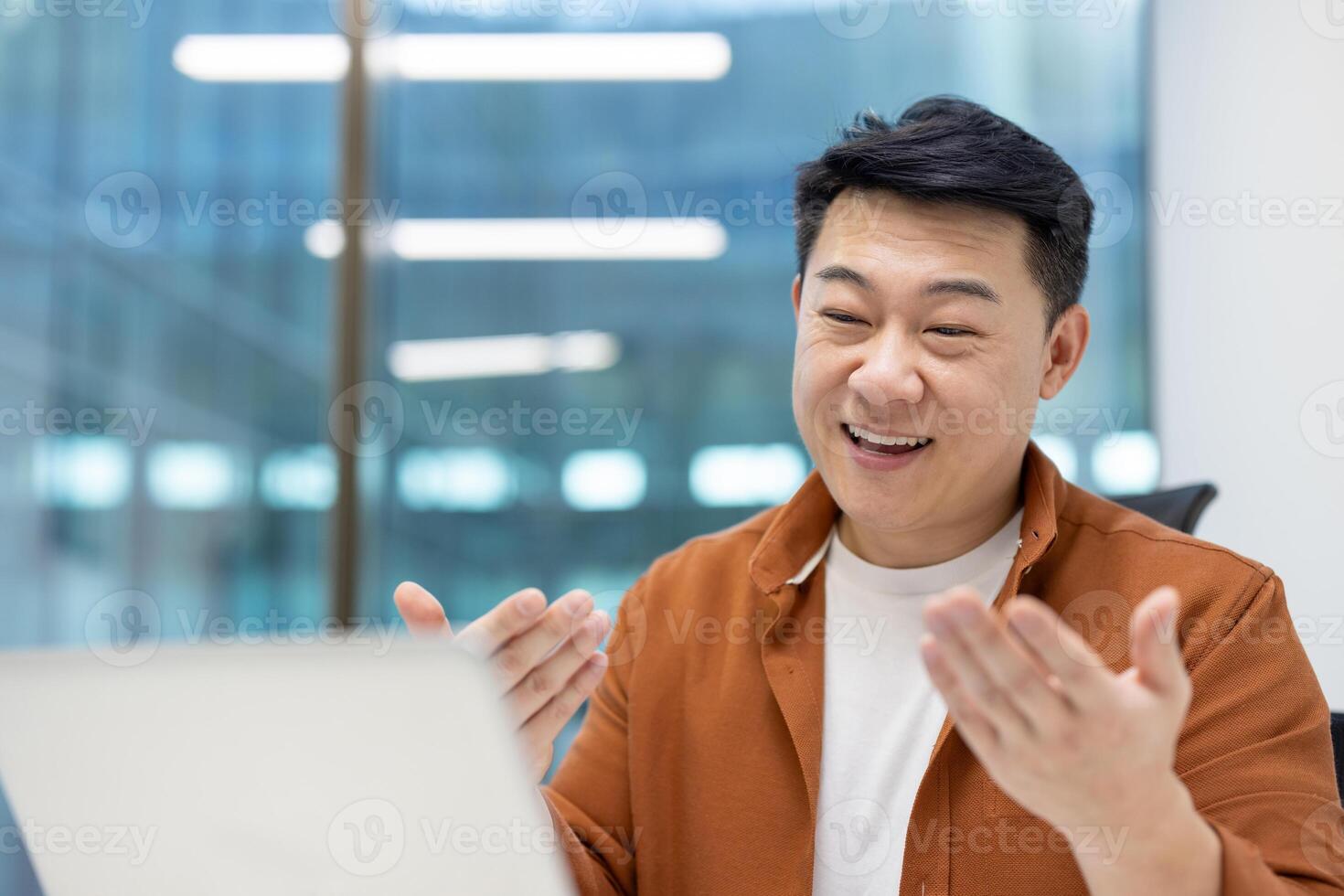 Asian man businessman engaged in call in office. He appears happy and communicative, suggesting positive interaction and successful business meeting. His open posture conveys enthusiasm. photo