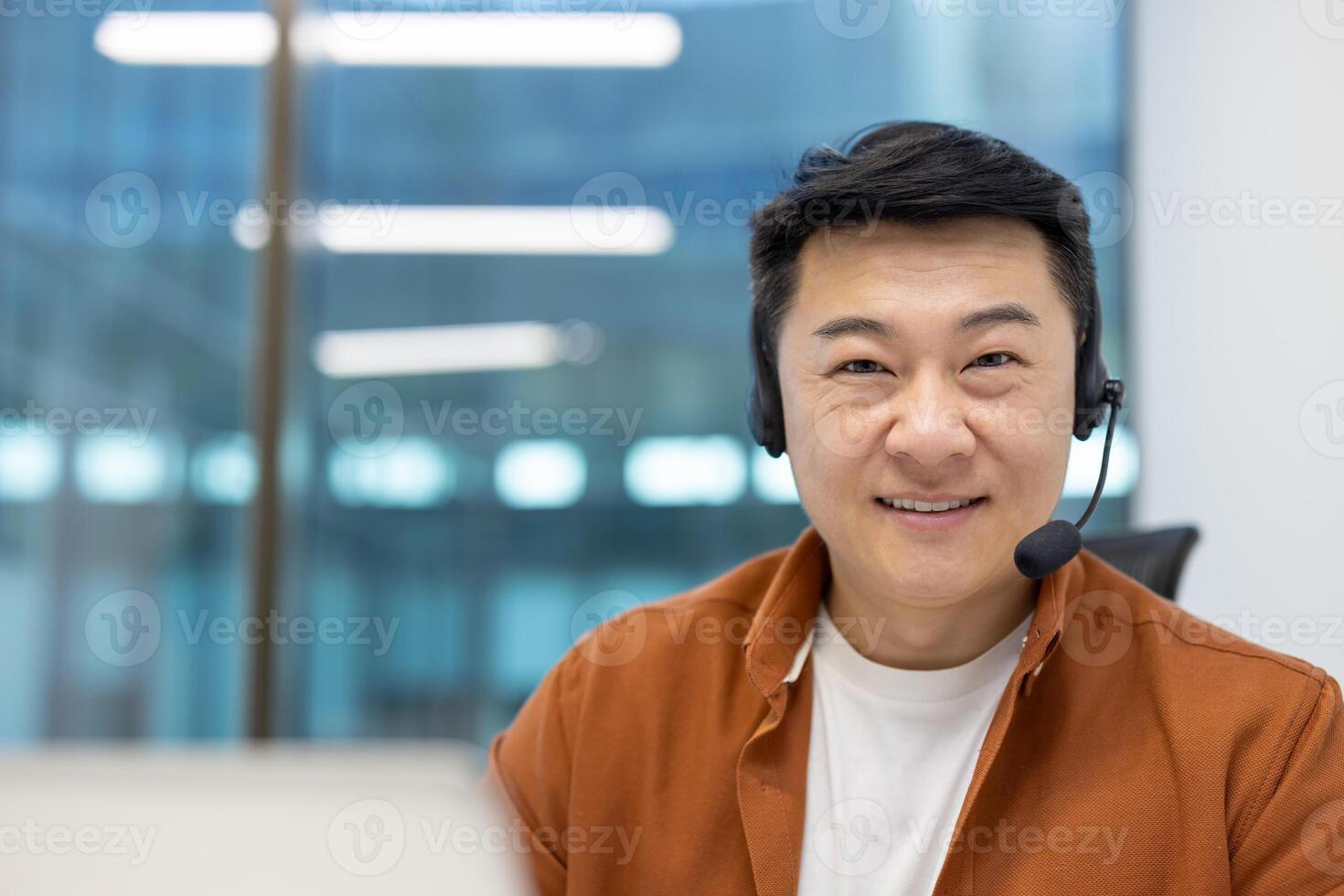 Asian man businessman wearing headset smiling in modern office. Demonstrates professional engagement in call or teleconference. Portrays confidence, digital communication, and work environment. photo