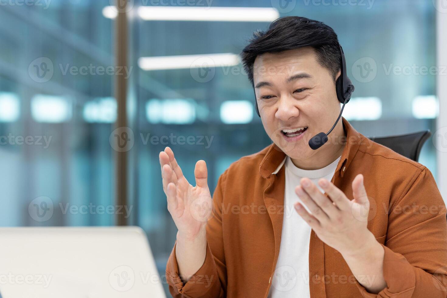 Mature Asian businessman with a headset communicating during an online meeting in a professional workspace, gesturing expressively, showcasing engagement and collaboration in virtual communication photo