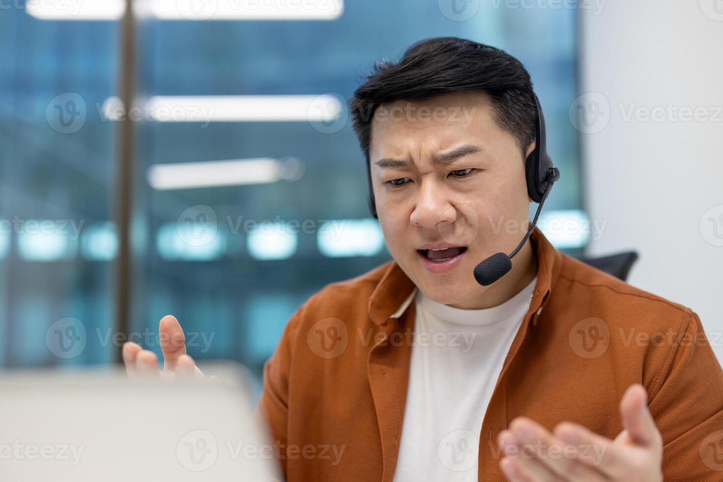 Asian man businessman with headset in office expressing concern during call. Engaged in call, online meeting, or customer service. Focused, interactive with phone setup. photo