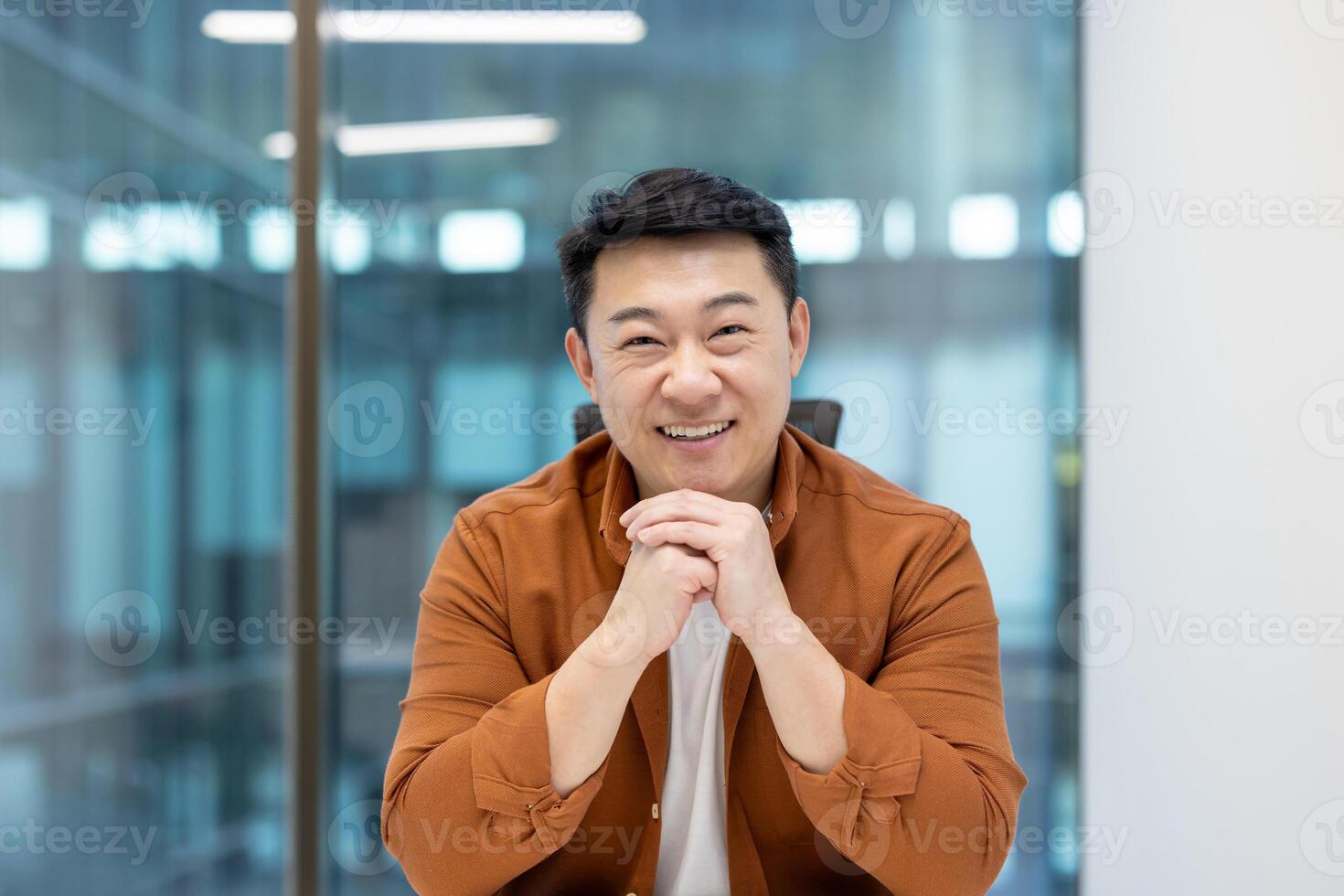 Close-up portrait of Asian businessman, man smiling and looking at camera, working inside office at workplace, mature experienced office worker, company worker. photo