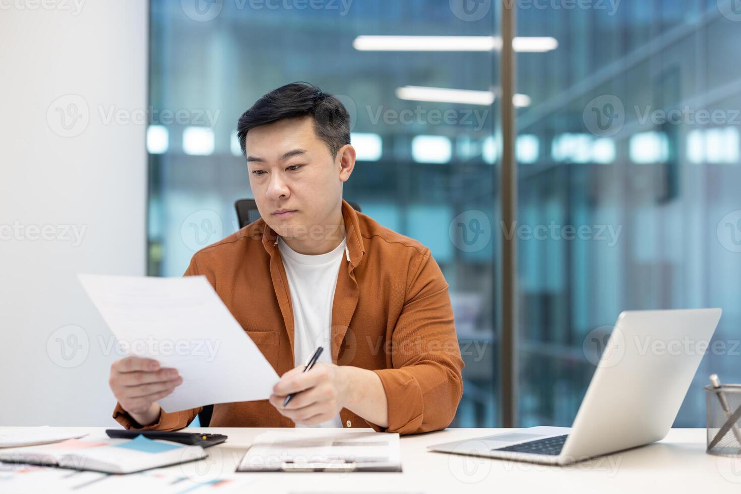 Serious man behind paperwork, mature financier checking investment contracts and reports. Successful Asian financier behind paperwork with notebook. photo