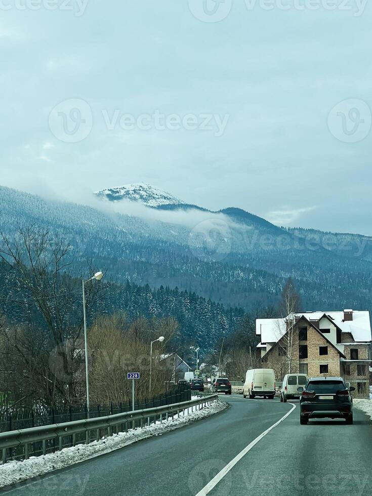 Scenic winter road with mountain view and rural architecture under cloudy sky photo