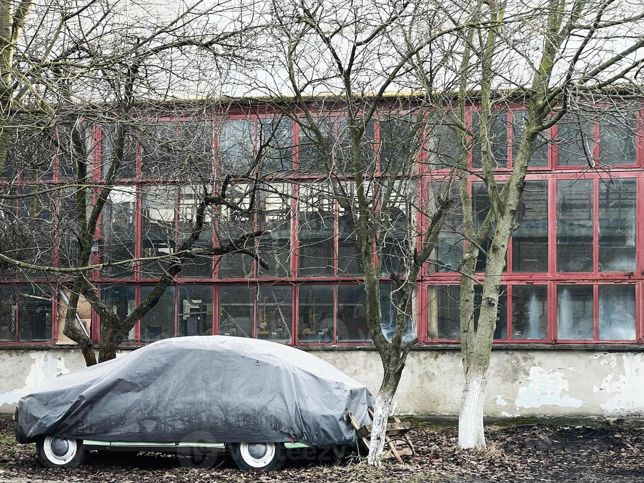Covered car near factory building with bare trees surrounding the scene photo
