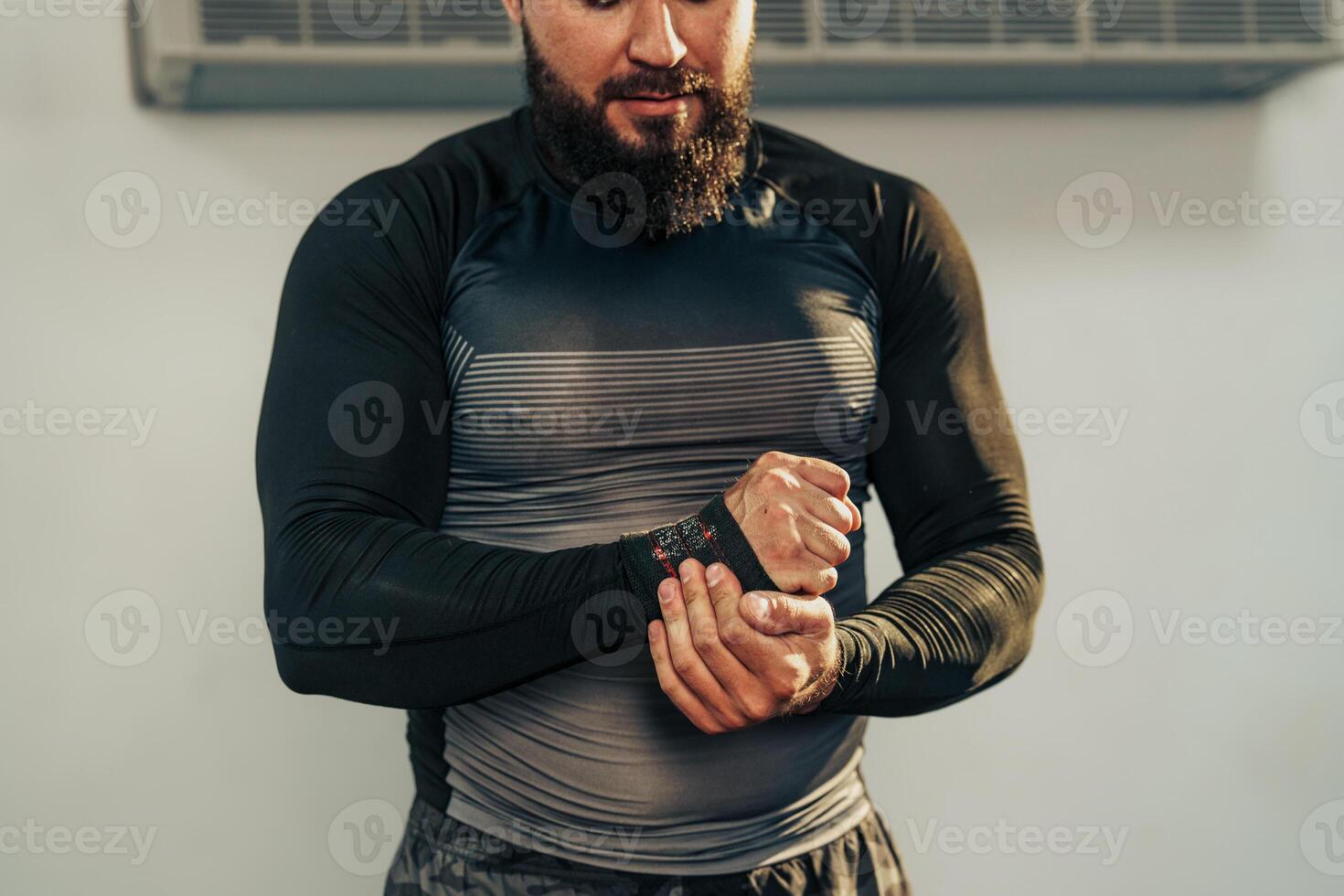 Man adjusts wrist support while preparing for workout in a gym setting with fitness equipment in the background photo
