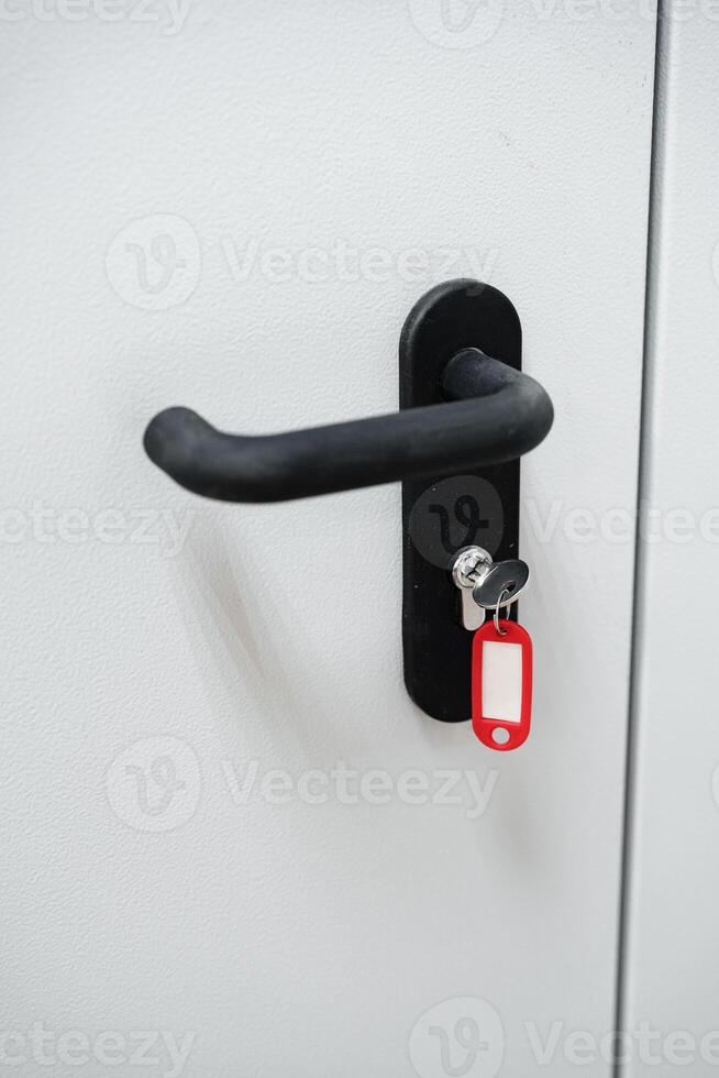 Key hanging on a red tag attached to a black door handle on a plain white door in a modern setting photo
