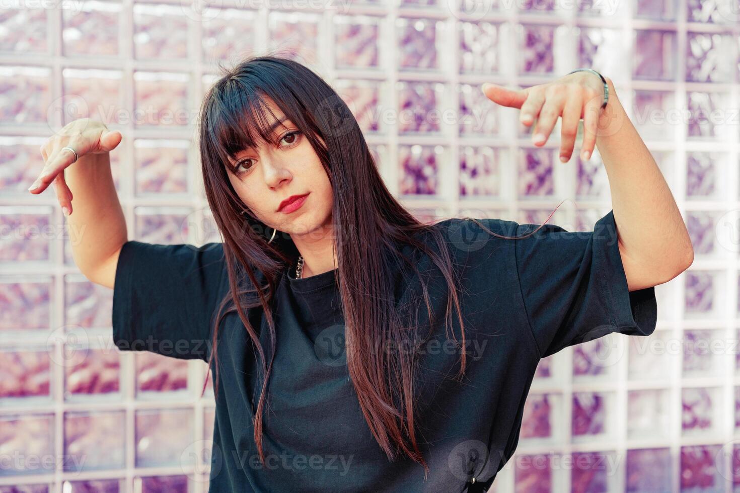 Young woman poses playfully in front of a textured glass wall during daylight in an urban location photo