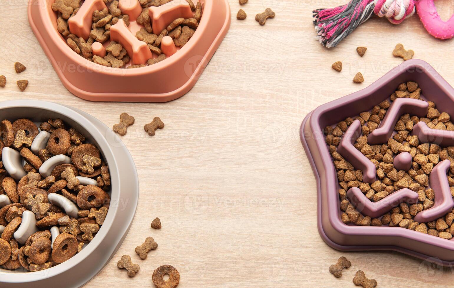 Different dry dog food in slow feeder bowl and toy on wooden table photo
