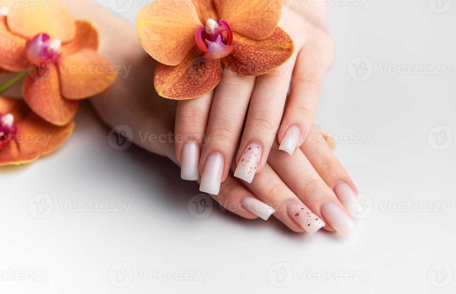 Woman showing stylish white nails with orange orchid decoration photo