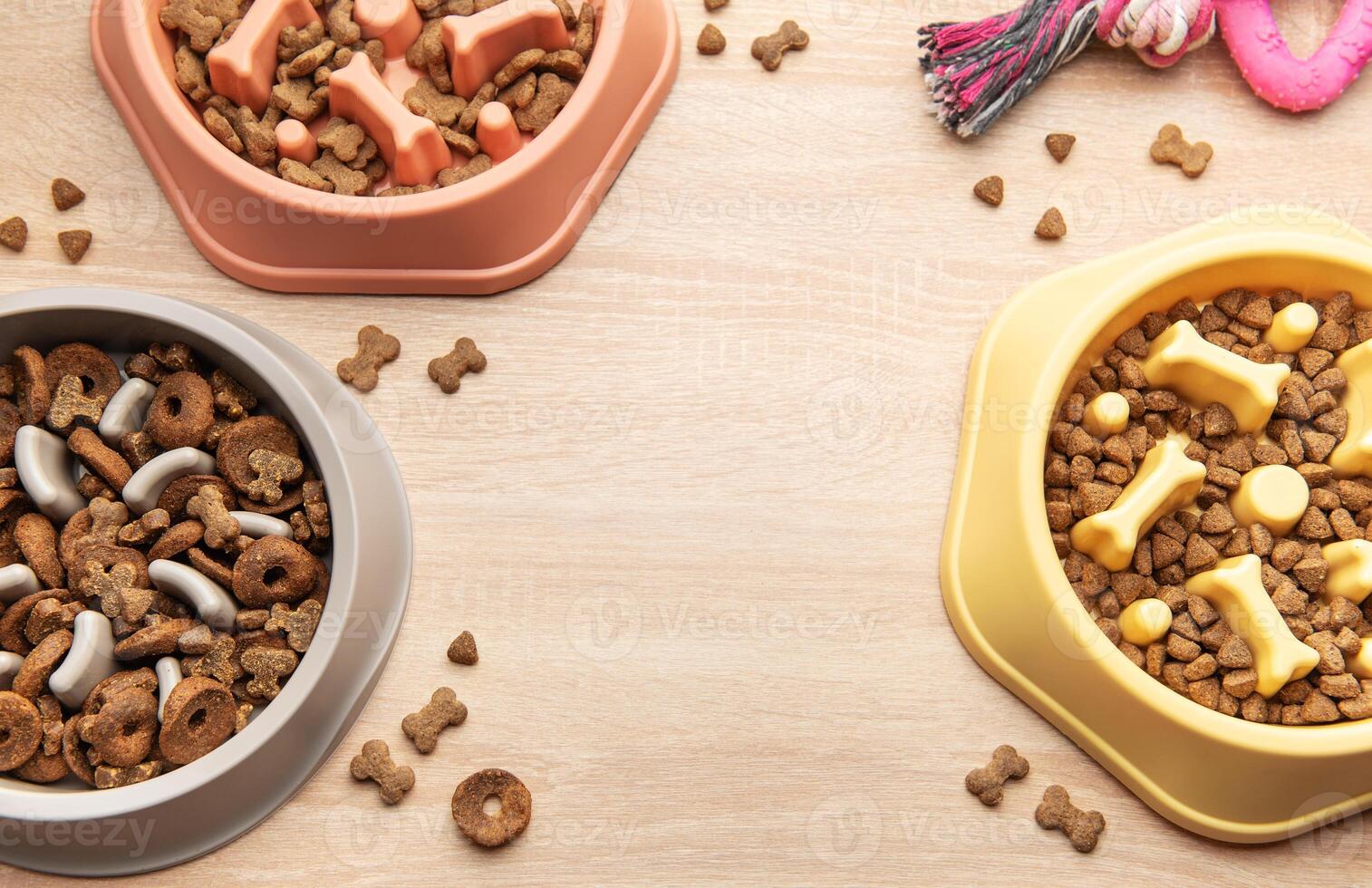 Different dry dog food in slow feeder bowls and toy on wooden table photo