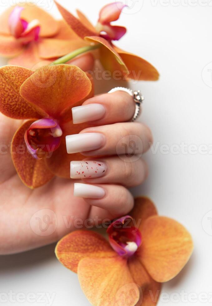 Woman hand showing stylish trendy nude manicure with orchid flowers photo