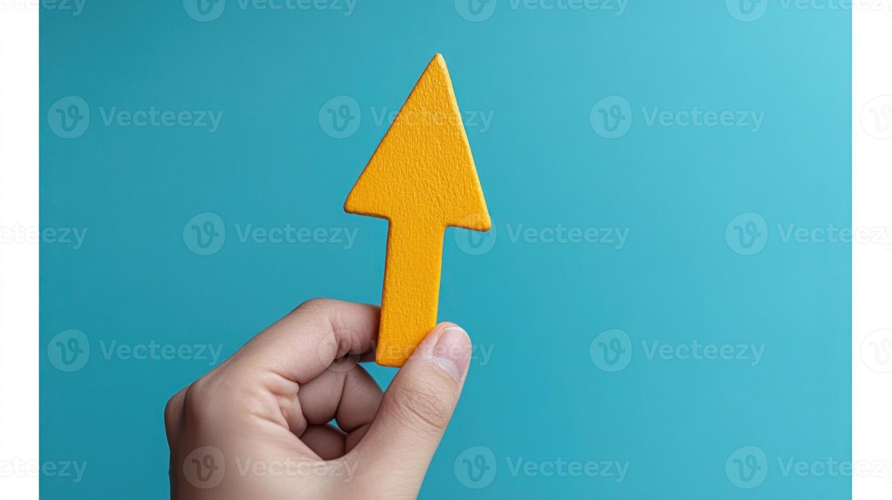 A hand is displaying a vibrant yellow arrow shape with a smooth finish against a blue backdrop photo