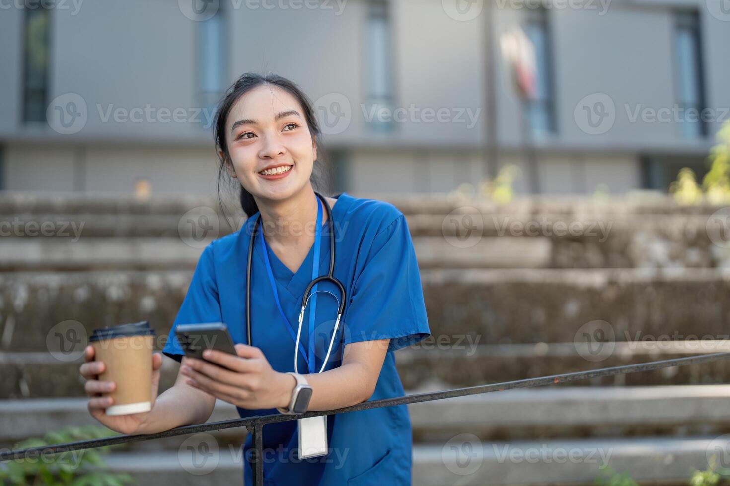Nurse with a coffee cup and smartphone, smiling while enjoying a break in a modern healthcare setting photo