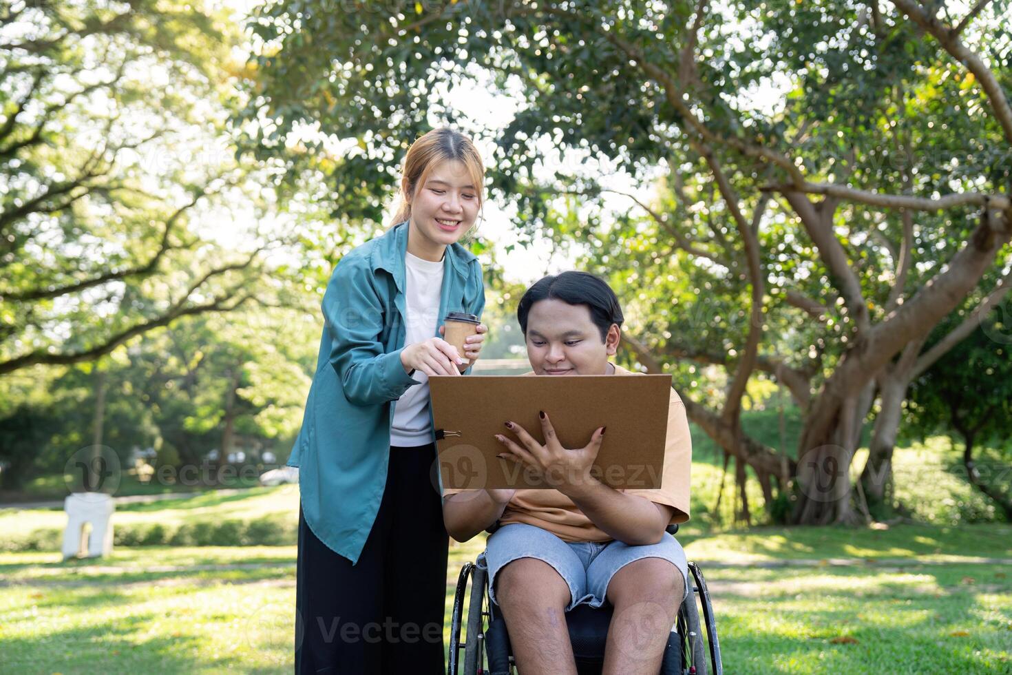 Disabled artist receiving guidance from instructor while creating art outdoors in a lush park photo