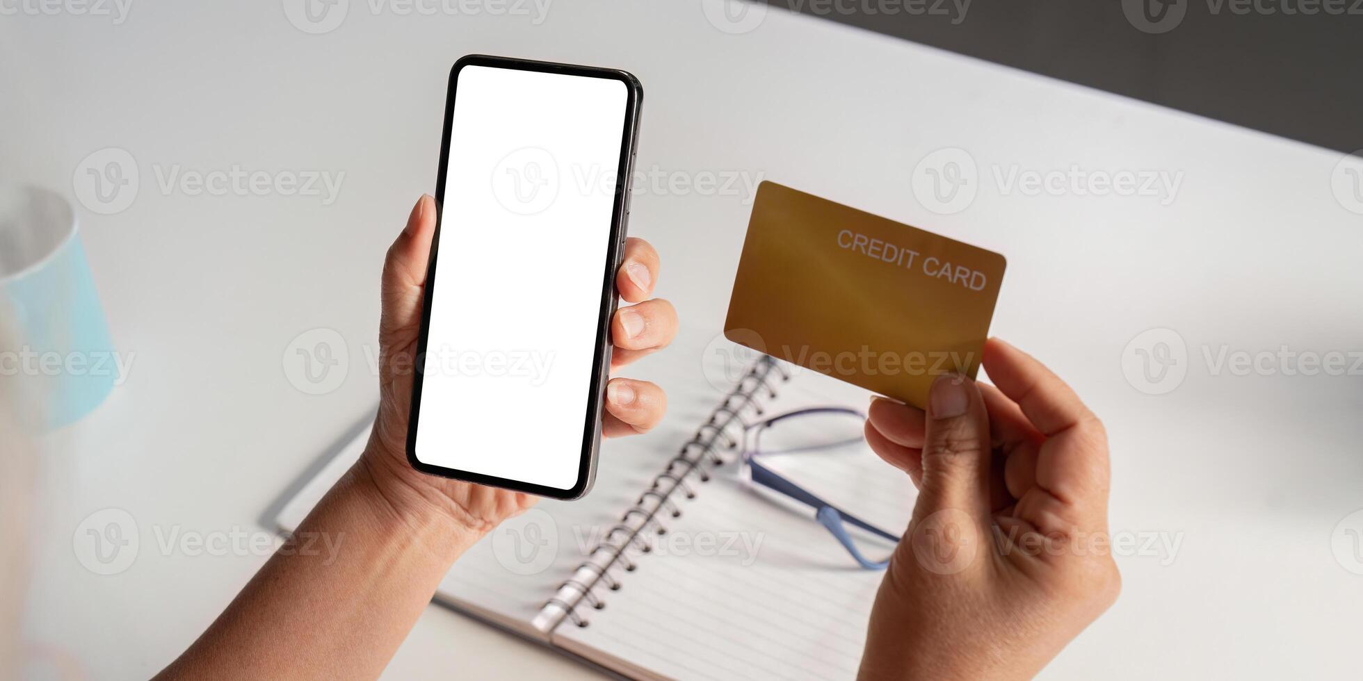 Elderly person holding a smartphone with a blank screen and a credit card over a table. photo