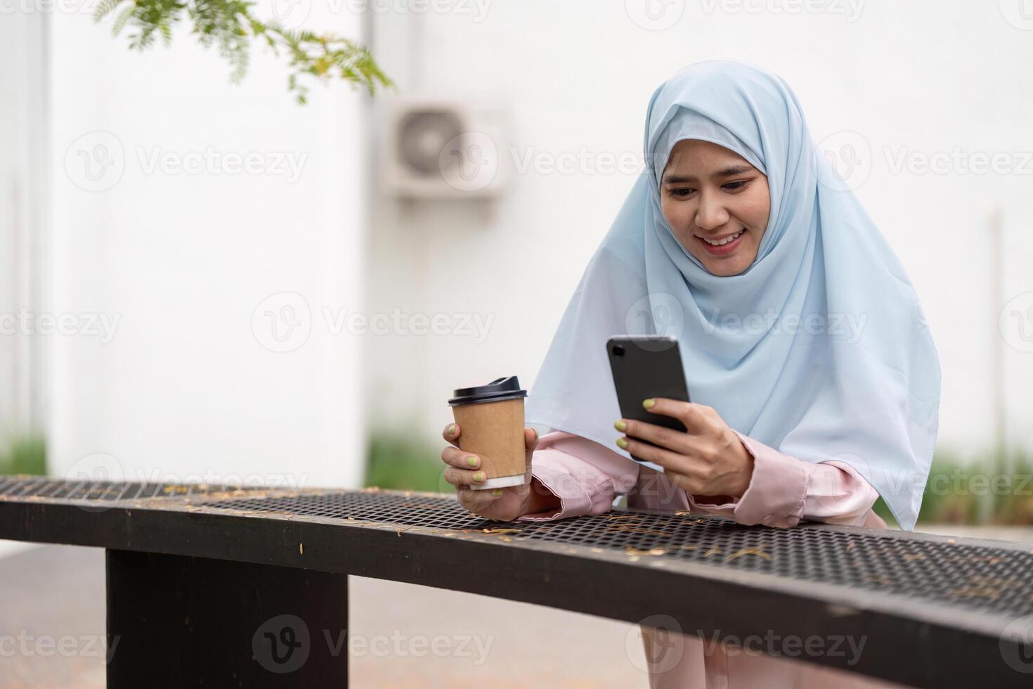 Muslim woman in hijab enjoying coffee while using smartphone for business photo