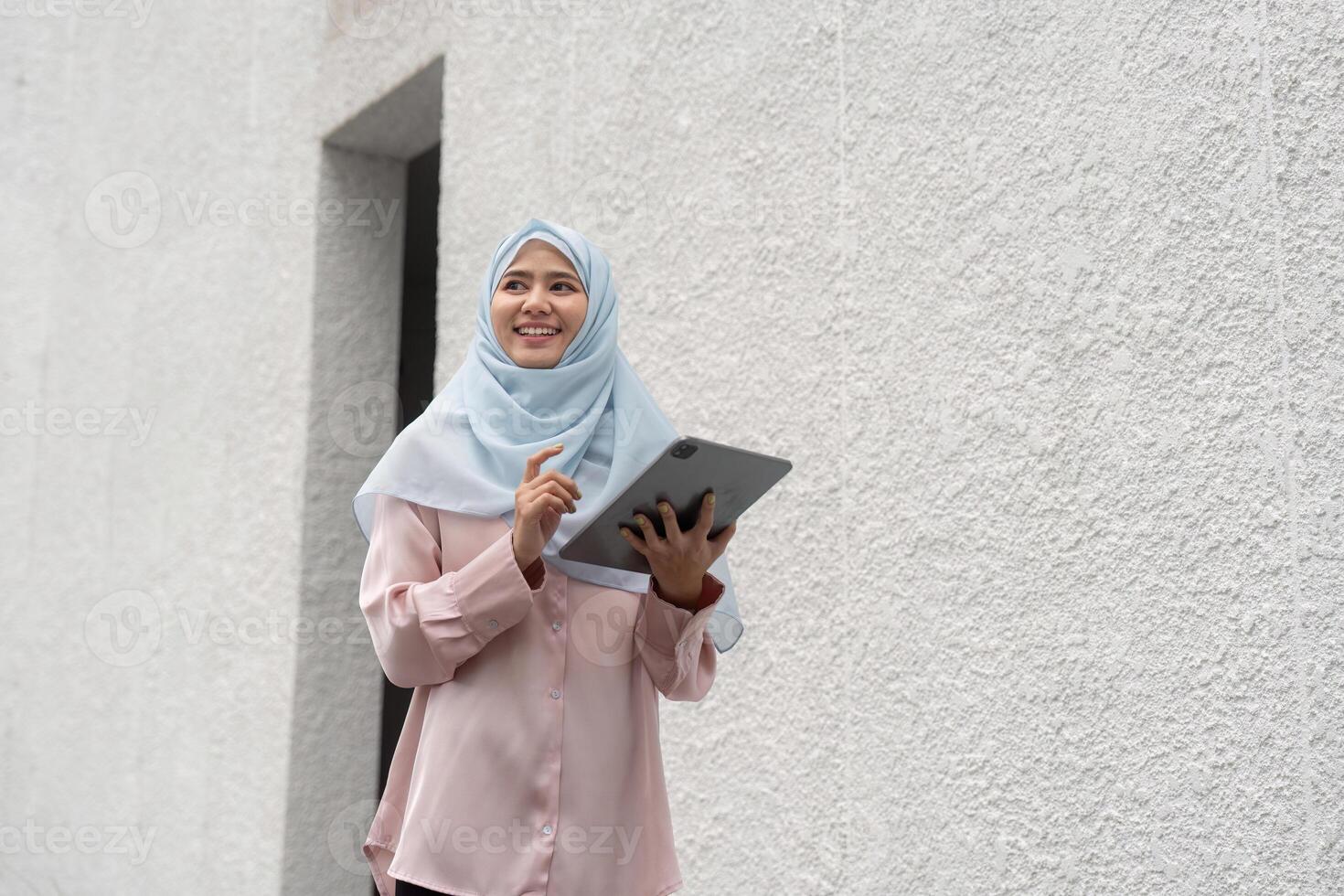Smiling Muslim woman using a tablet in a modern business environment. photo