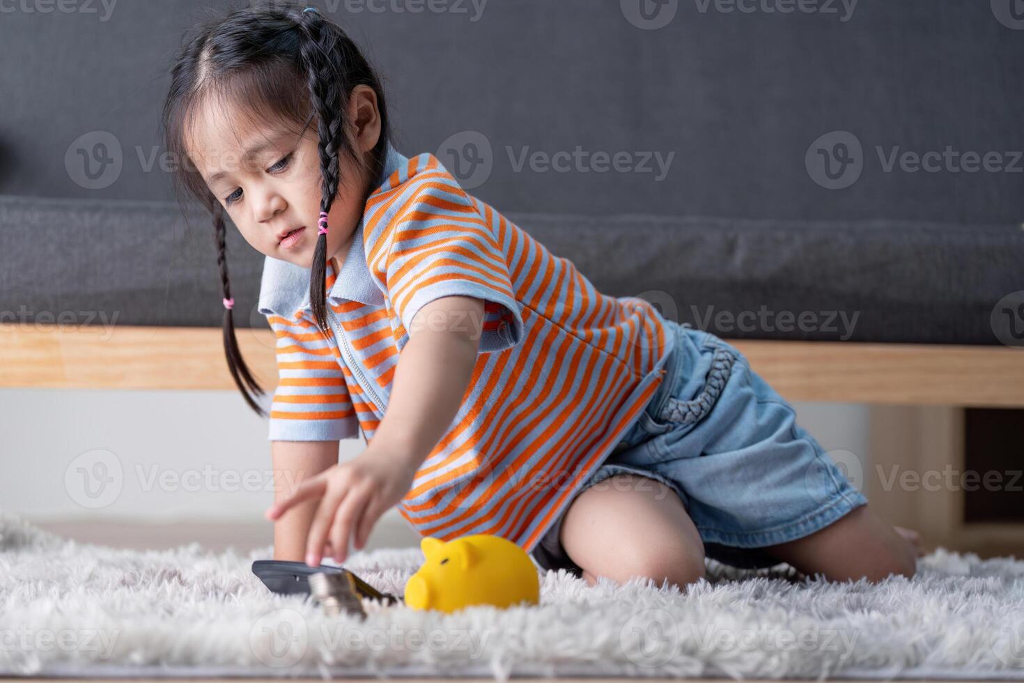 Young girl learning to save money with a yellow piggy bank and coins at home, fostering financial skills and independence. photo