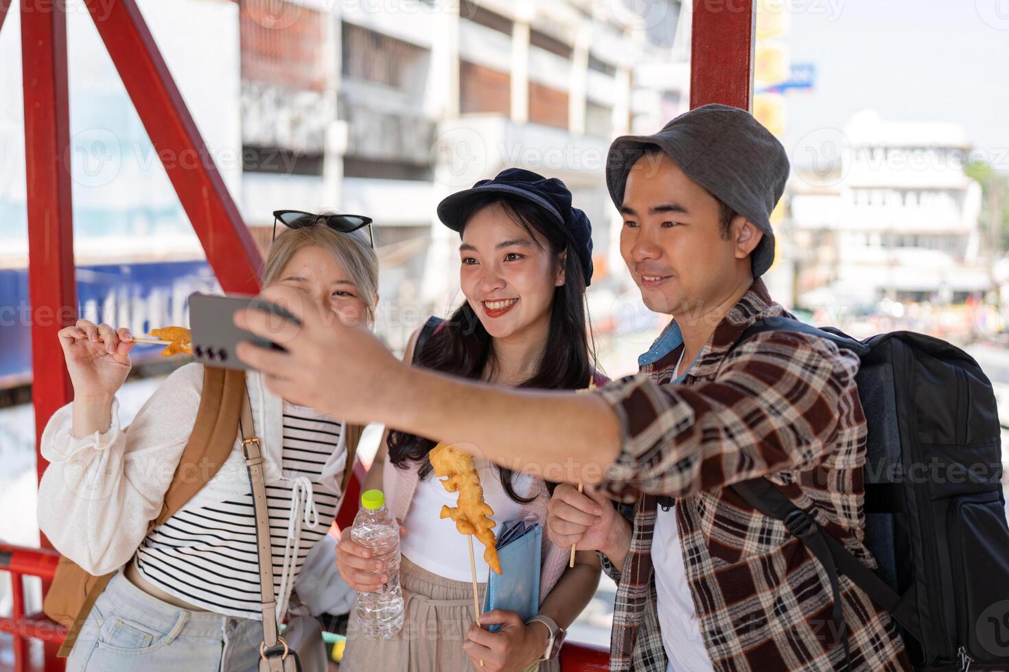 Young Asian friends taking a selfie while enjoying street food at a vibrant market, celebrating travel and friendship. photo