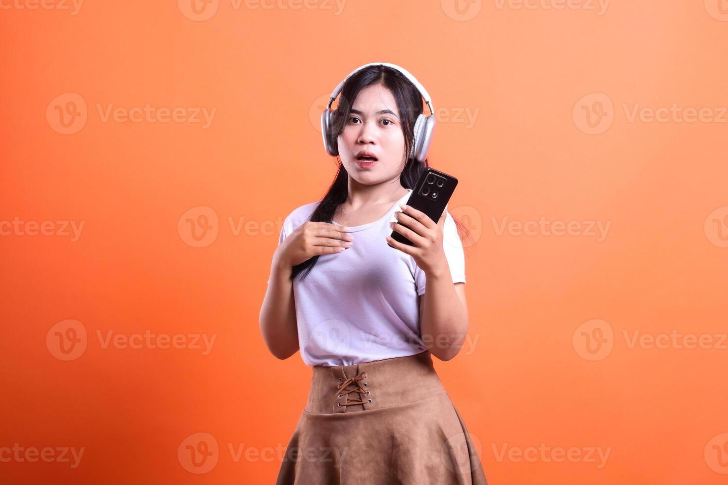 Young woman with headphones holding a smartphone on orange background isolated photo