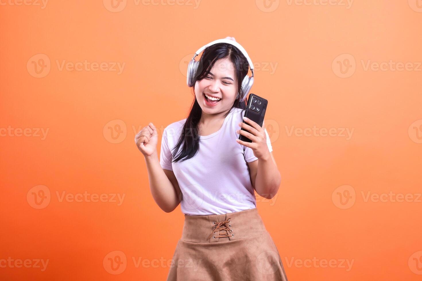 Woman with headphones listening to music on her phone in orange background photo