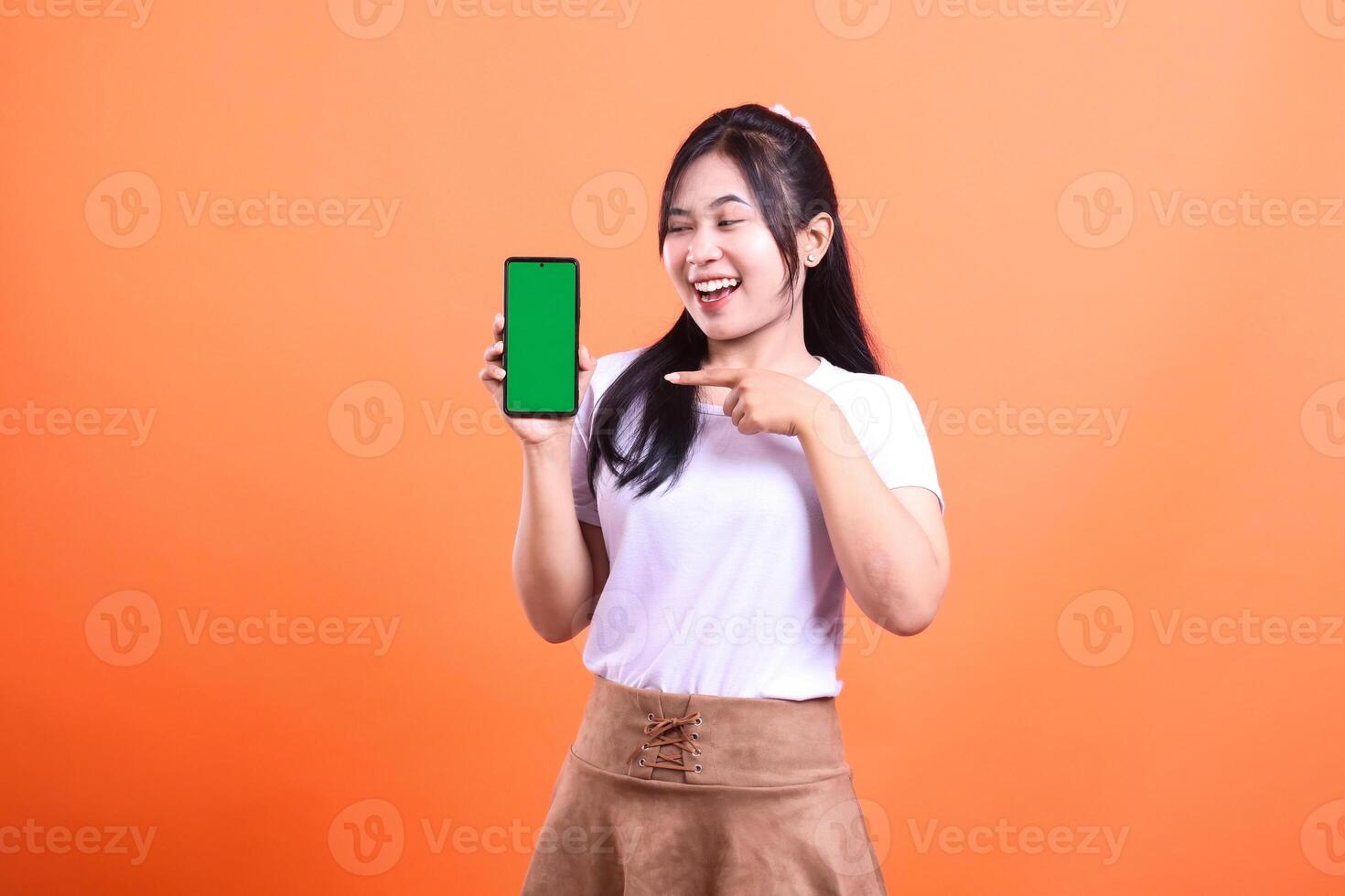 A woman presenting a smartphone with green screen in an orange background photo