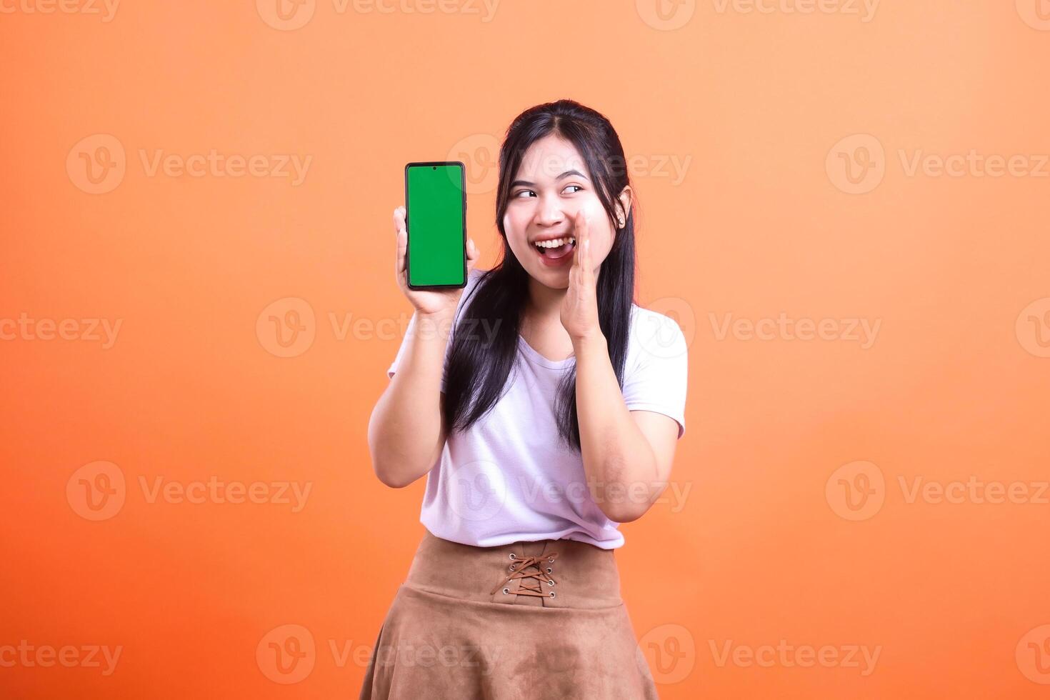 A smiling woman with dark hair holding up a cell phone with a green screen photo