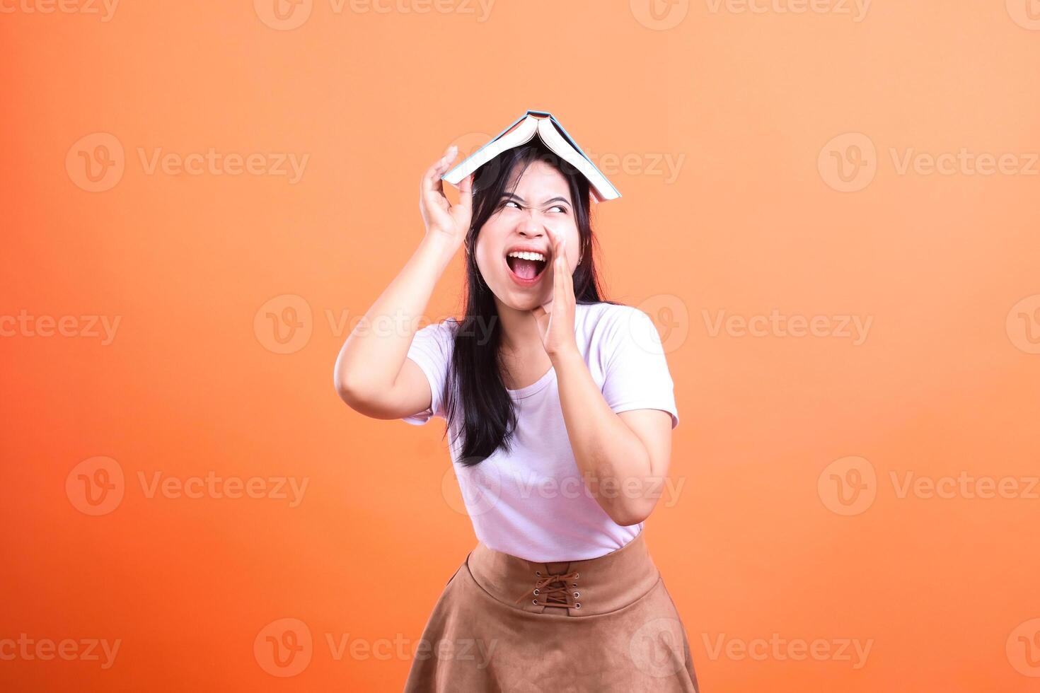 A woman with a book on her head with an orange background is yelling for help isolated on orange background photo