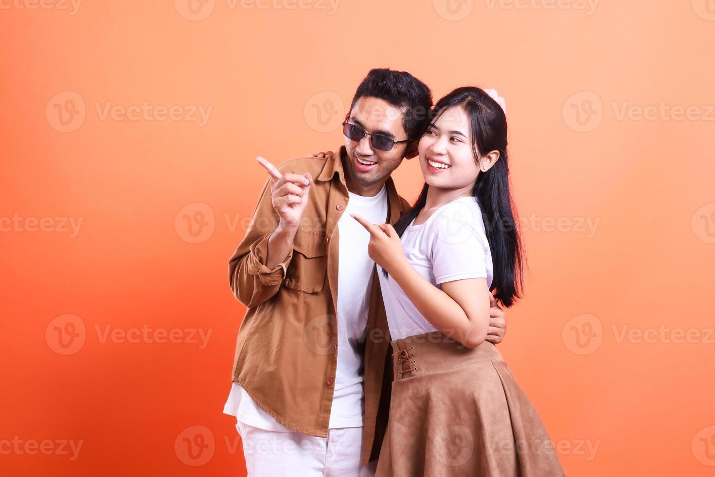 a couple asia of teenage lovers cheerful expression pointing right where the man and woman stand facing each other romantically. isolated on orange background photo