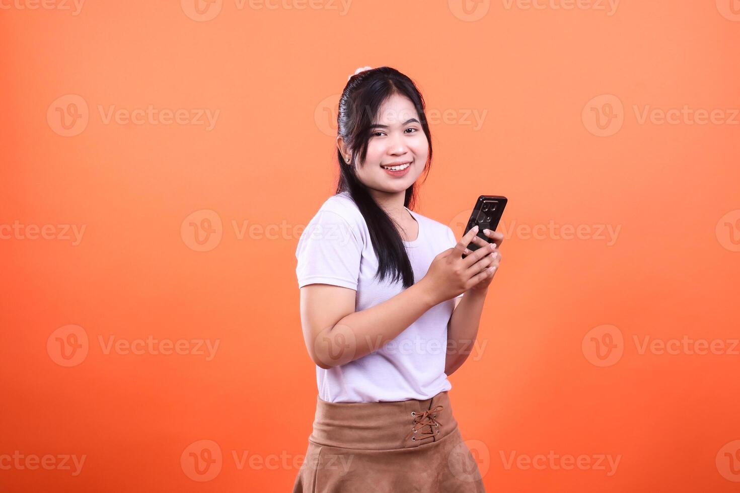 A smiling person in a white shirt is holding a phone on an orange background photo