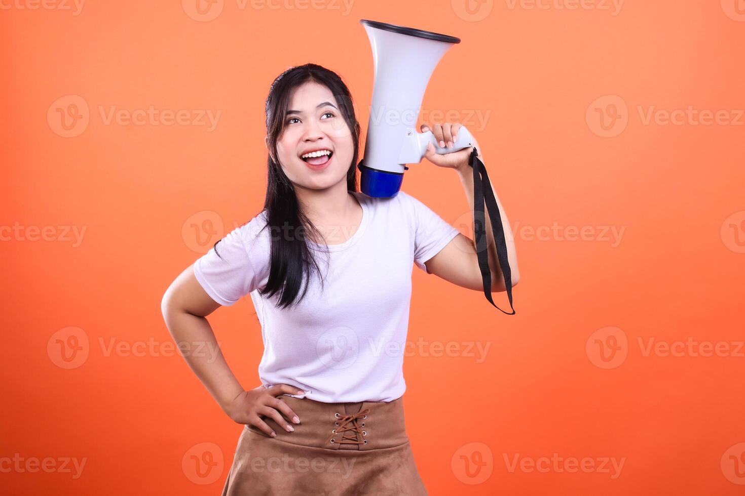 A woman with a megaphone on an orange background announcing loudly looking up photo