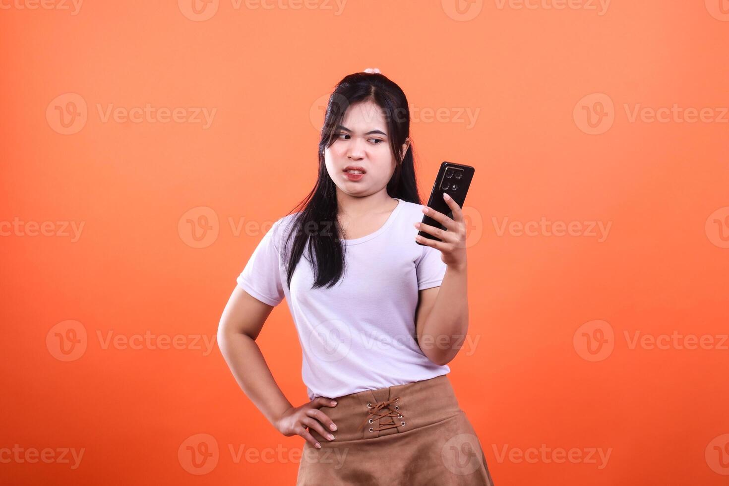 A person is holding a cell phone in front of an orange background while wearing a white t-shirt photo