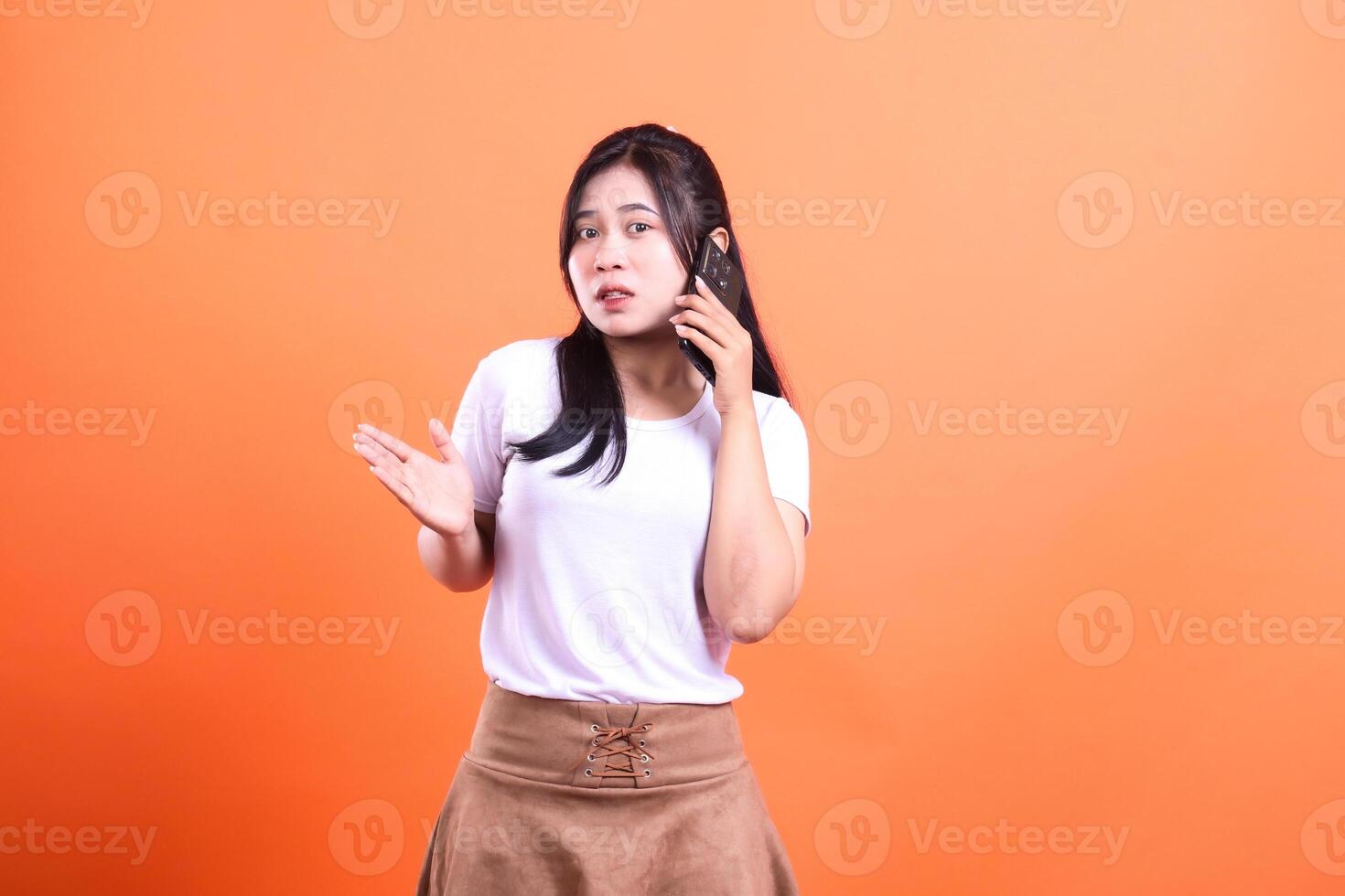 A young woman with long dark hair is having a phone conversation on an orange background photo