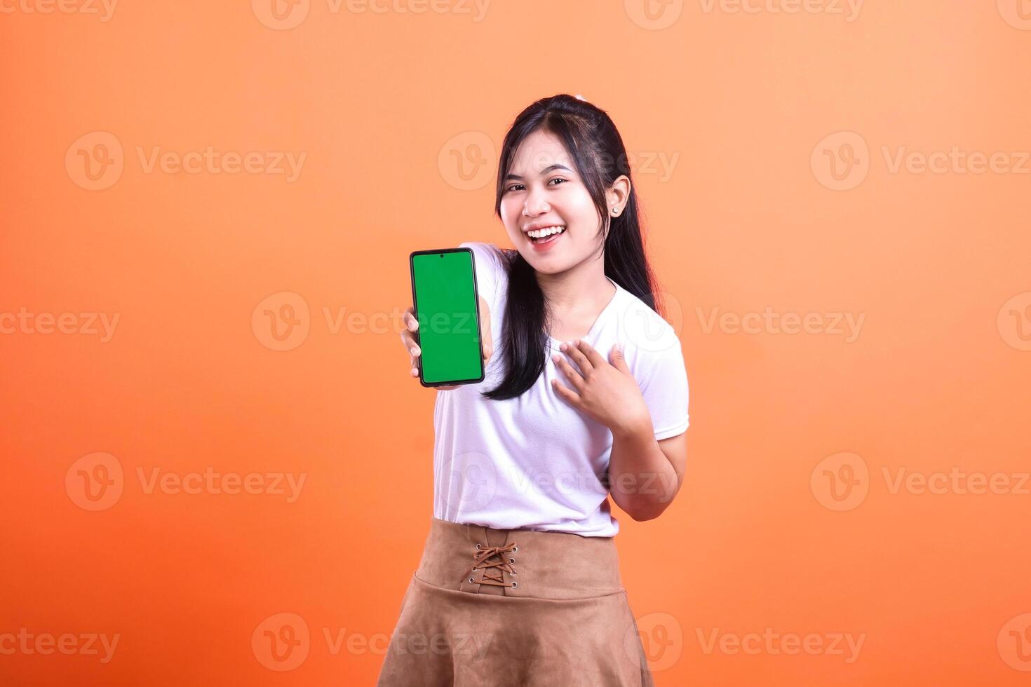 A woman presents a cellphone with a green screen against a bright orange background photo