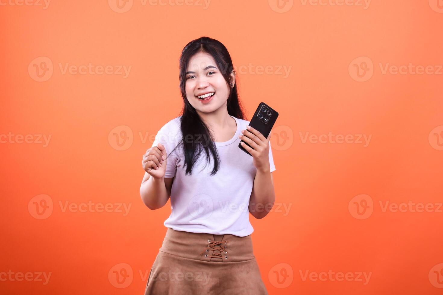 Smiling woman with cellphone isolated on orange background posing for a photograph photo