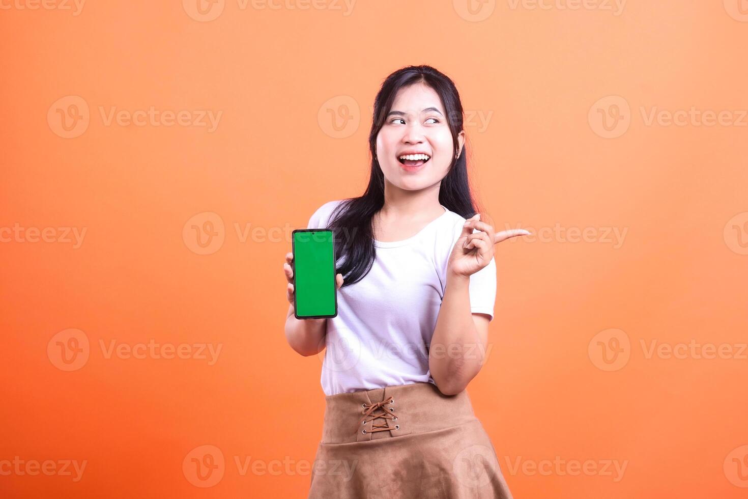 Woman presenting a mobile phone with a green screen on an orange background photo
