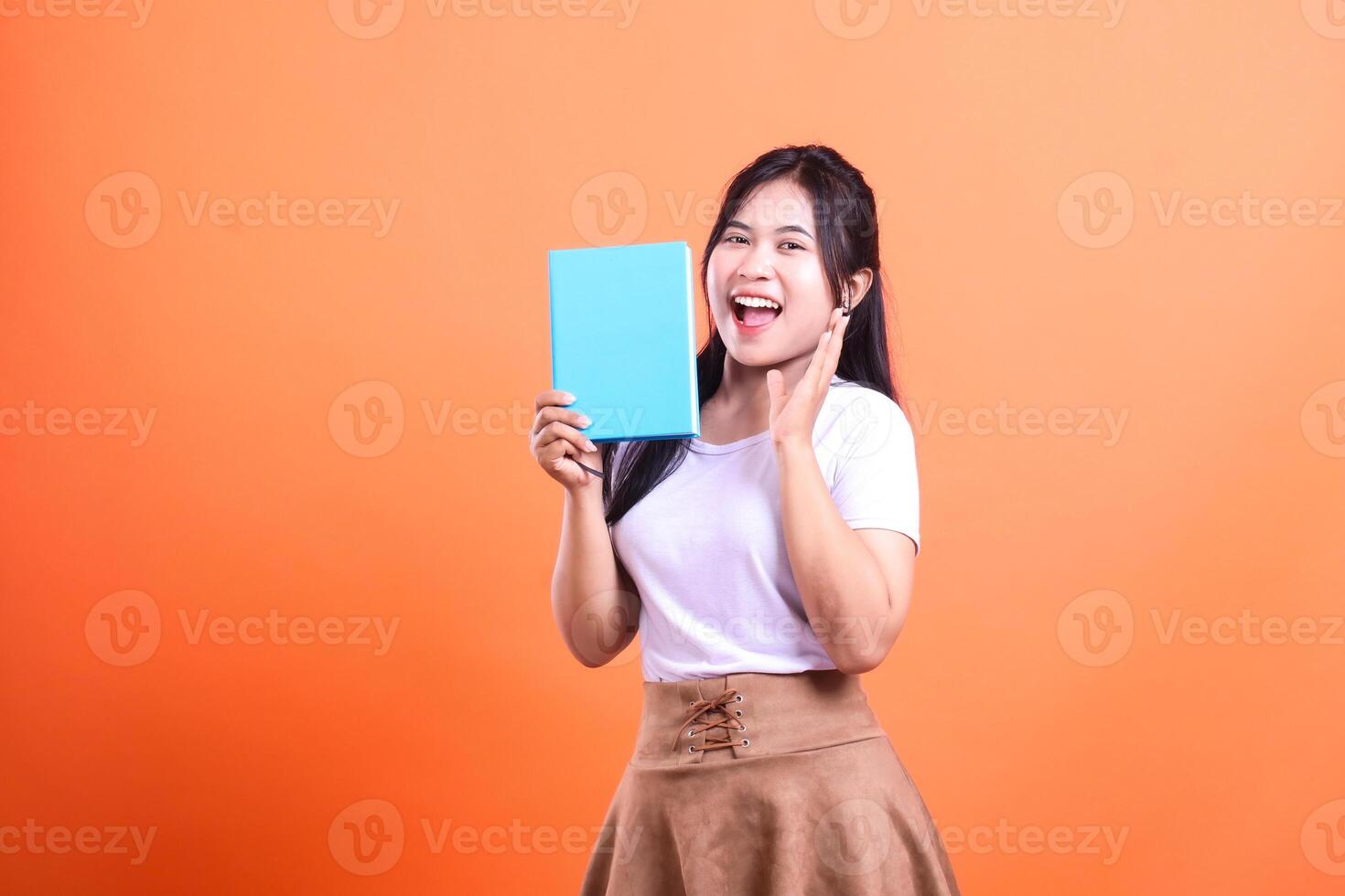 A woman is holding a book up with a surprised expression on an orange background while showing a book photo