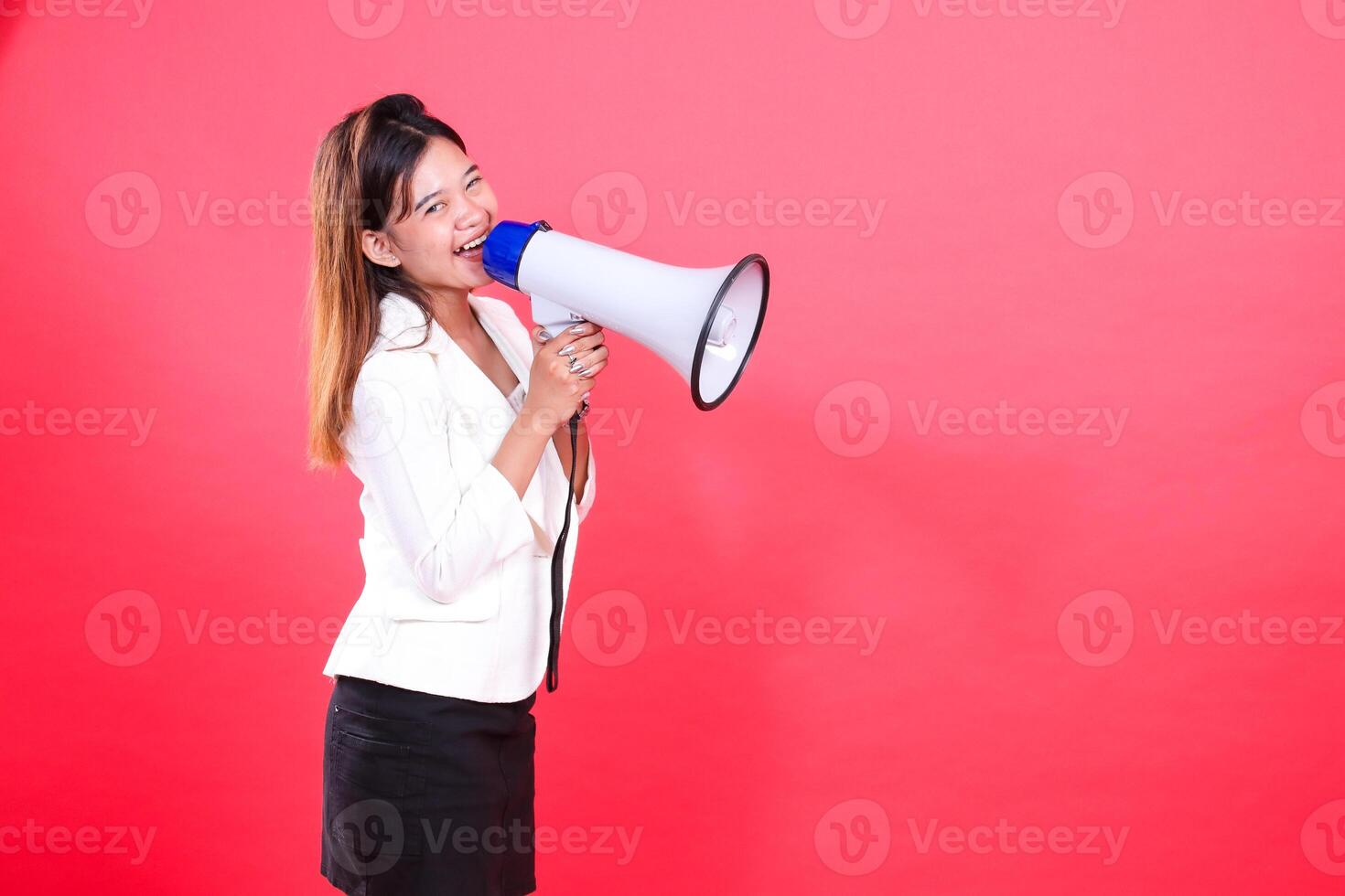 A woman wearing a white blazer and a black skirt is speaking into a white megaphone, the figure is isolated on a red background photo