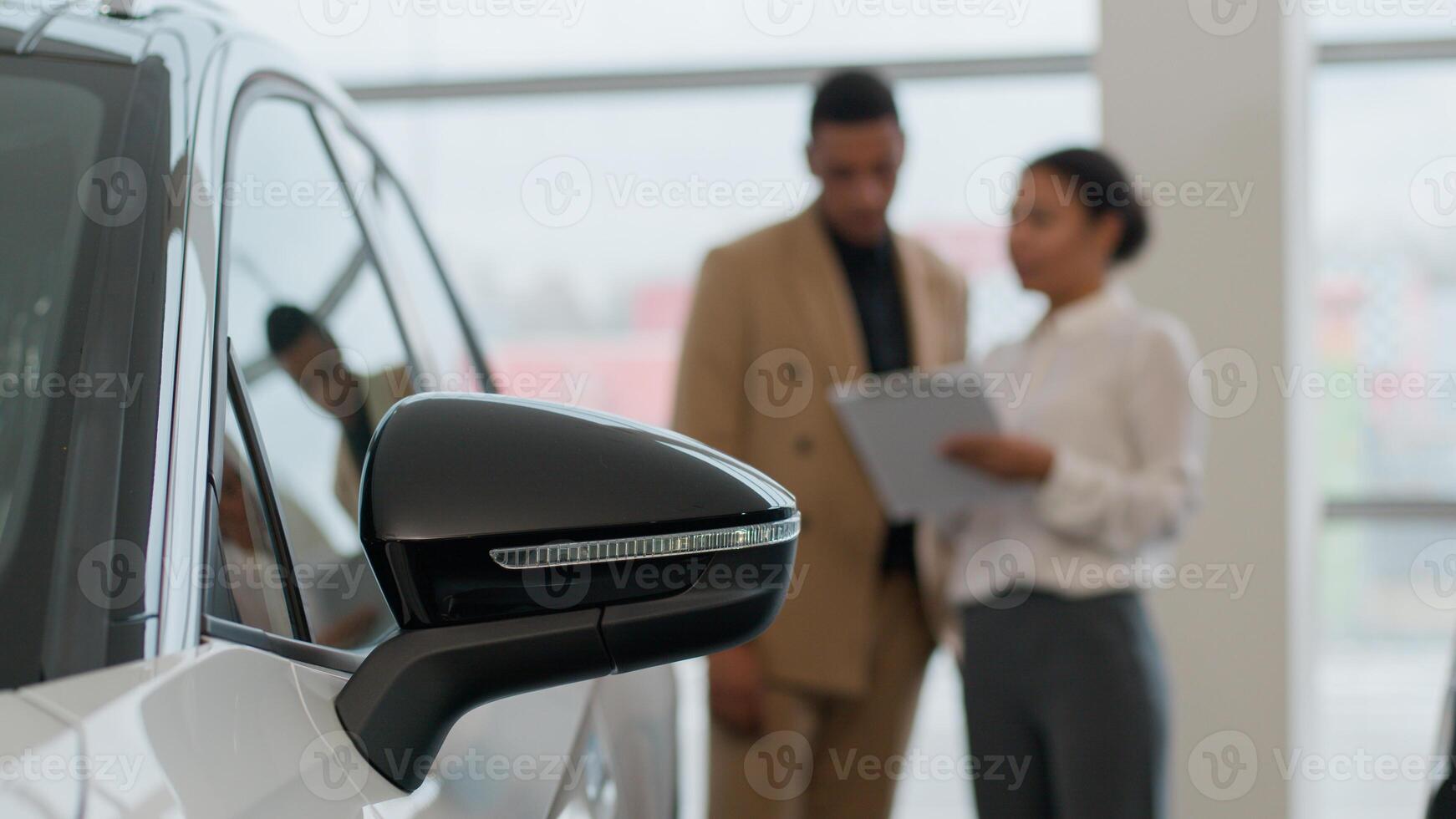 Close up wing mirror of modern car woman seller talk to buyer blurry on background auto dealer and client business man loan credit deal selling vehicle at dealership buying new automobile in showroom photo