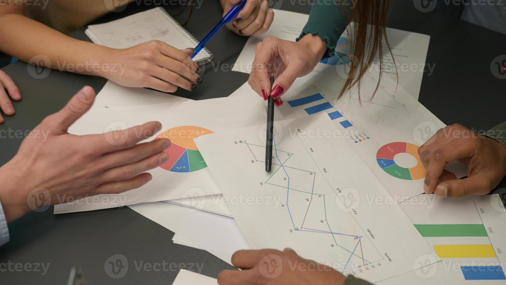 Close up table with papers documents unknown group of business men women discuss marketing research results review sales statistics data information analysis graphs charts planning strategy at office photo