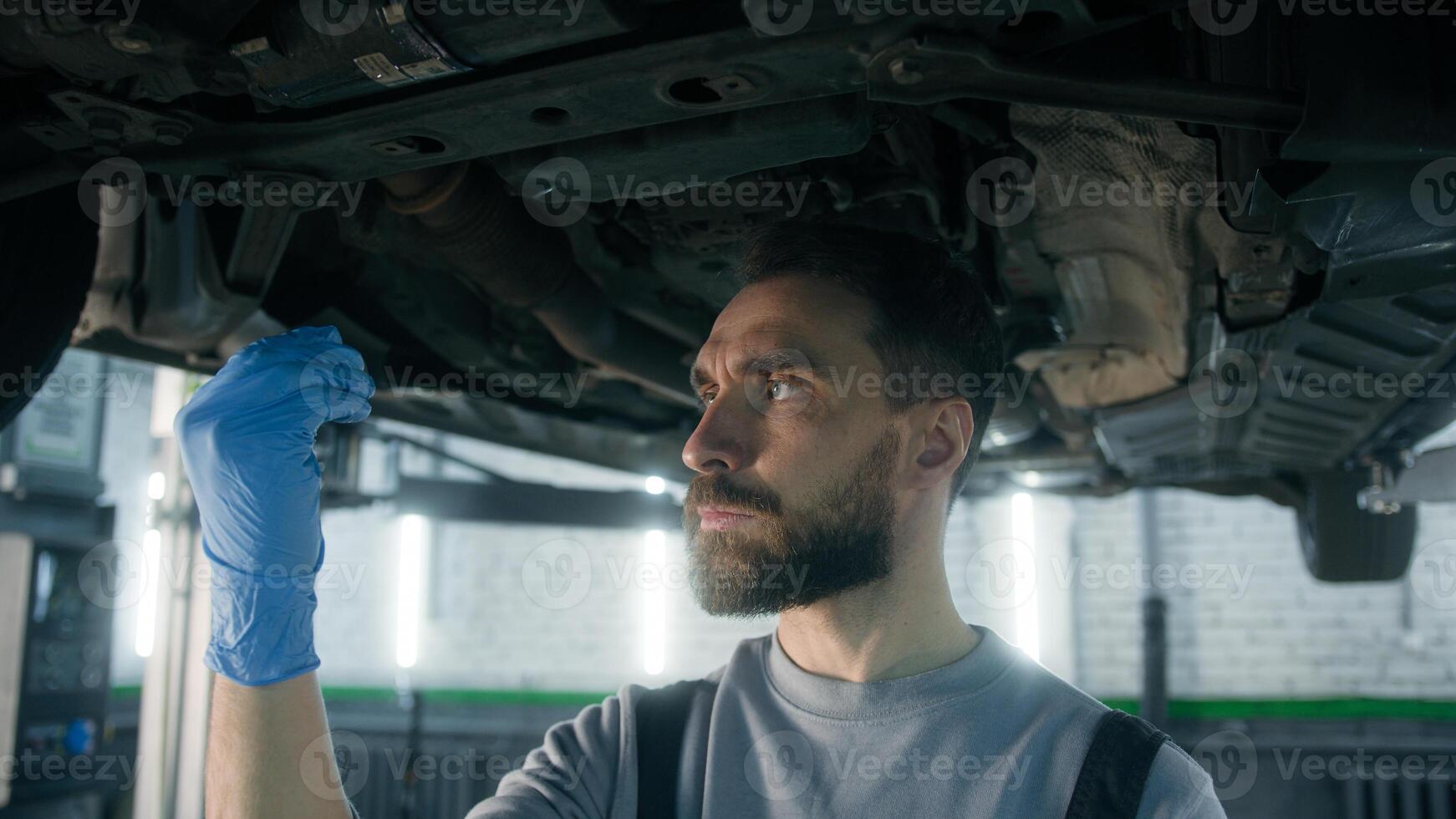 Auto mechanic Caucasian man repairman technician work underneath car lifting vehicle at garage auto repair service station checking truck fuel oil gasoline condition automobile maintenance diagnostics photo