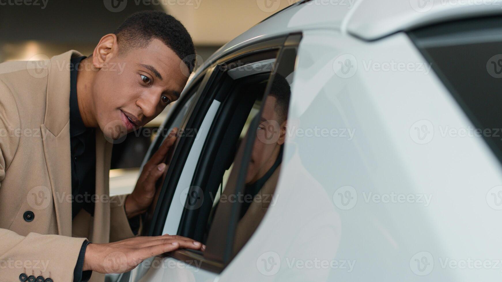 African American ethnic man smiling customer client looking inside car salon in dealership store male owner businessman buyer touching automobile vehicle review dreaming new luxury modern auto buying photo